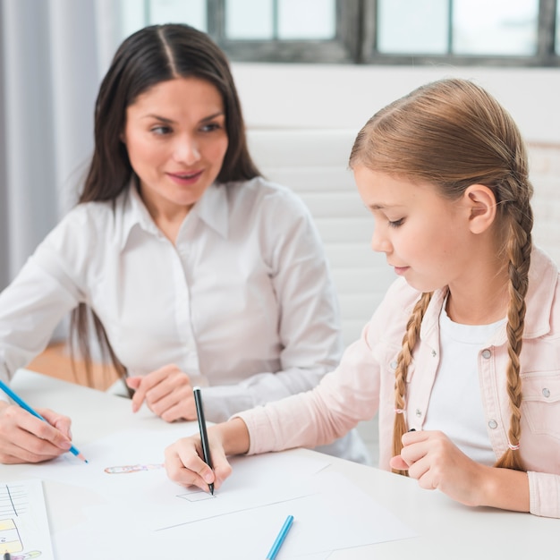 Free photo female psychologist looking at girl drawing with colored pencil