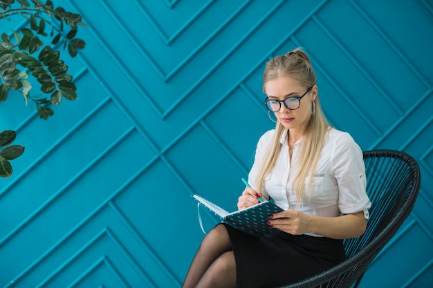 펜으로 일기에 디자인 파란색 벽 쓰기에 앉아 여성 심리학자
