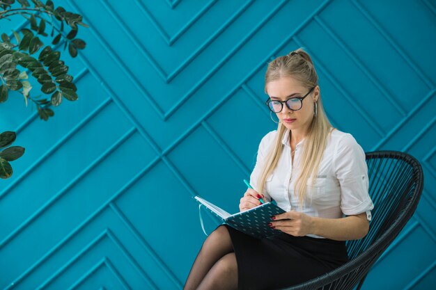 Female psychologist sitting against design blue wall writing on diary with pen