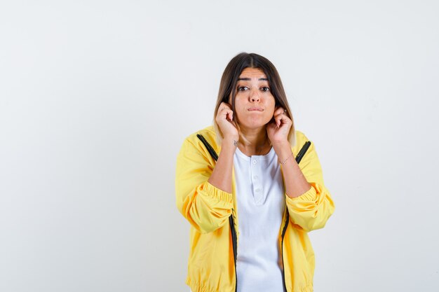 Female pulling down her earlobes in t-shirt, jacket and looking careful , front view.