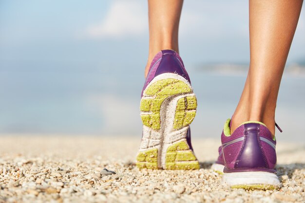 female purple sneakers stands on shell beach, wears sport shoes. Sport and healthy lifestyle concept