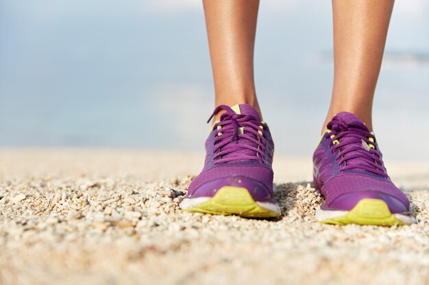 여성 보라색 운동화는 쉘 비치에 서서 스포츠 신발을 신습니다. 스포츠와 건강한 라이프 스타일 컨셉