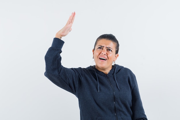 Female raising hand in hoodie and looking confused. front view.