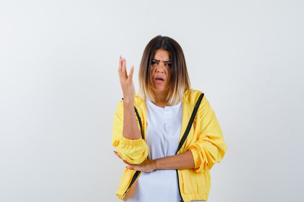 Female raising hand in questioning manner in t-shirt, jacket and looking puzzled. front view.