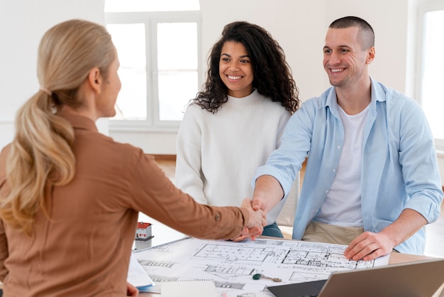 Female realtor handshaking couple to congratulate them on their new house