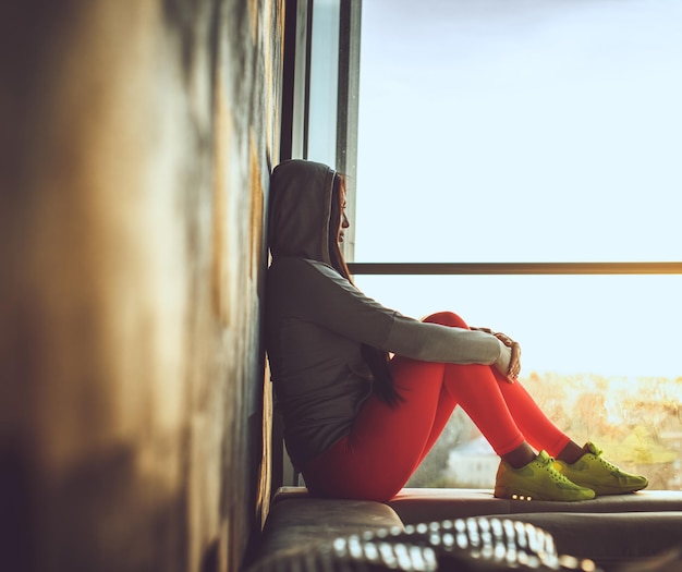 Free photo female in red pants and yellow shoes sitting near window.