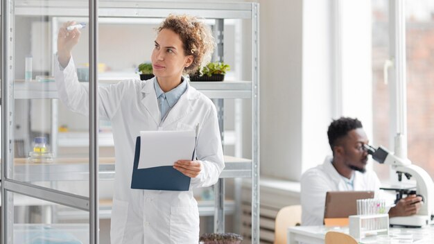 Female researcher with clipboard in the biotechnology laboratory and male colleague