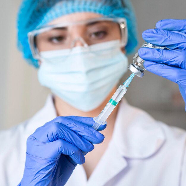 Female researcher with safety glasses and medical mask  holding syringe