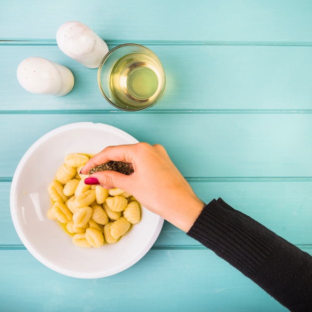 Foto gratuita la mano della femmina aggiungendo condimento sulla pasta di gnocchi