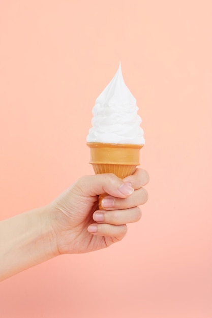 Female's hand holding delicious soft ice cream in a crispy waffle cone on a pink scene