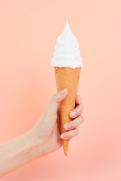 Female's hand holding delicious soft ice cream in a crispy waffle cone on a pink scene