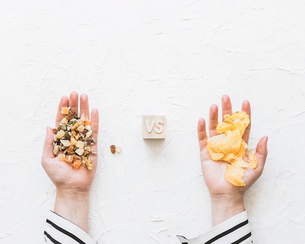 Бесплатное фото Рука женщины держит сухофрукты против чипсов картофеля на текстурированном фоне
