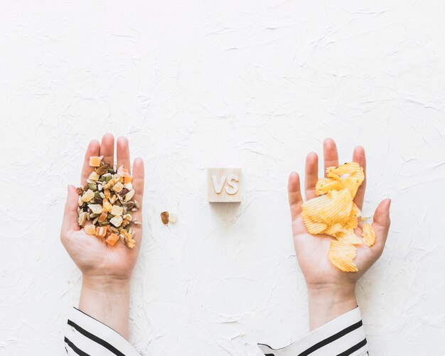 Female's hand holding dryfruits versus potatoes chips on textured backdrop