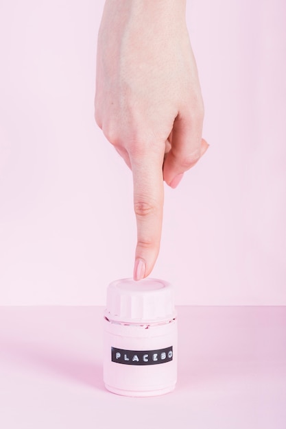 Женская рука, указывающая на бутылку плацебо на розовом фоне