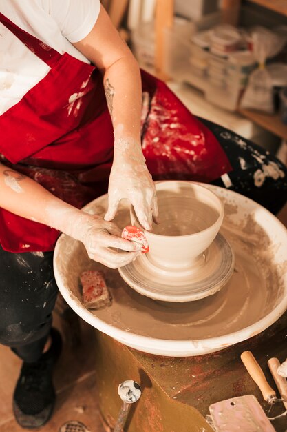 Female's hand smoothing out the bowl with flat tool on potters wheel