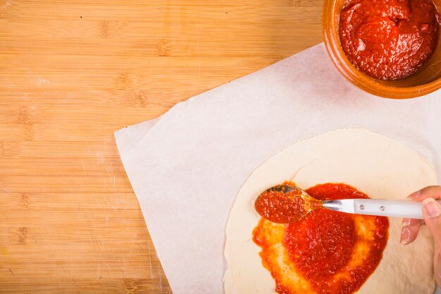 Female's hand spreading sauce on dough