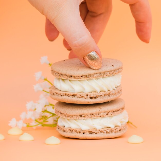 Female's hand with golden nail polish taking macaroon against colored backdrop