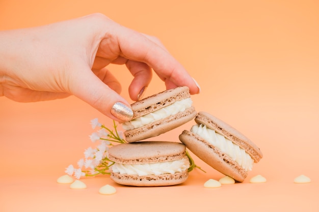 Female's hand with golden nail varnish taking macaroon against colored backdrop