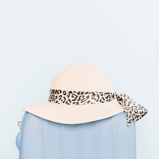 Female's hat on plastic luggage travel bag against blue background