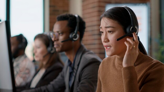 여성 판매 대리인이 고객과 전화 통화를 하여 고객 지원 서비스에서 사람들을 돕습니다. 콜센터 워크스테이션, 헬프데스크에서 도움을 주기 위해 헤드폰을 사용하는 여성.