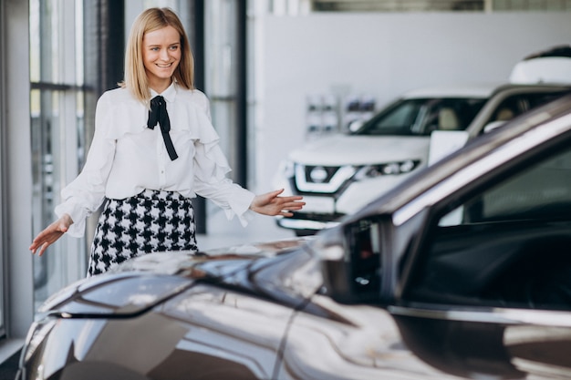 Female salesperson at a car showroom standing by the car