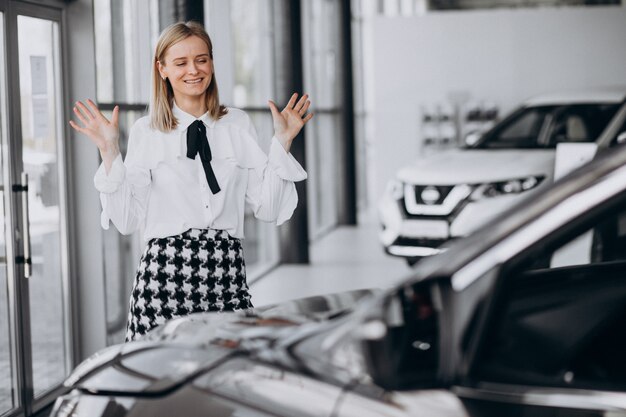 車のそばに立って車のショールームで女性営業担当者