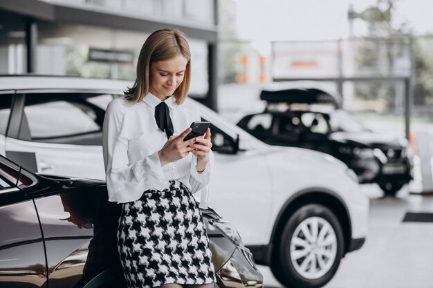 車のそばに立って車のショールームで女性営業担当者