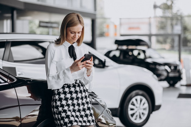 Female salesperson at a car showroom standing by the car