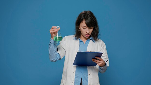 Female scientist analyzing liquid in beaker and chemistry files, wearing white coat and working on pharmaceutical development experiment. Chemist using substance in laboratory jar and papers.