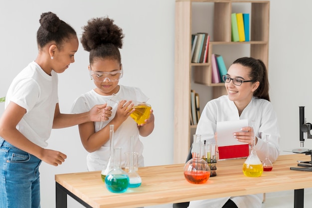 Female scientist watching girls experimenting with chemistry