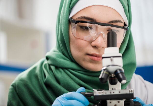 Женщина-ученый с хиджабом смотрит в микроскоп