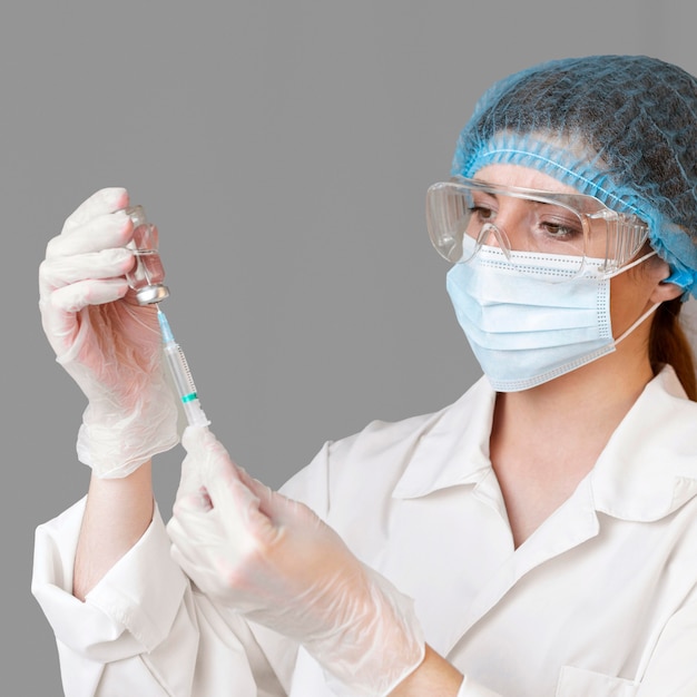 Женщина-ученый в защитных очках и сетке для волос держит шприц