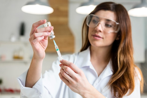 Female scientist with safety glasses holding syringe with vaccine in the lab