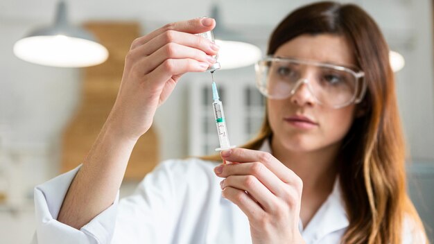 Female scientist with safety glasses holding syringe with vaccine