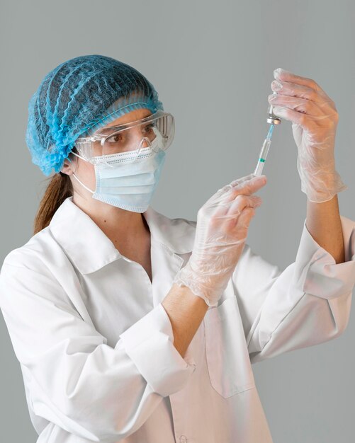 Female scientist with safety glasses and medical mask holding syringe