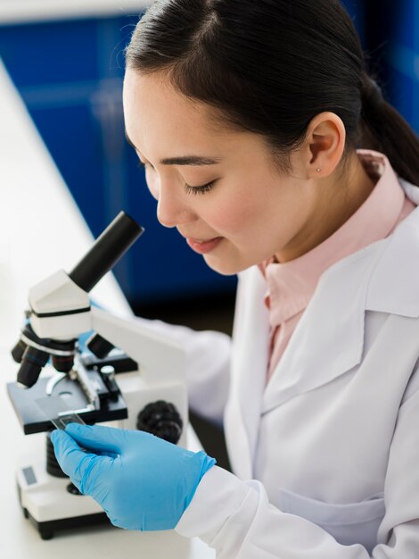 Женщина-ученый с хирургическими перчатками смотрит в микроскоп