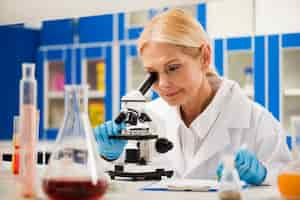 Free photo female scientist with surgical gloves looking through microscope