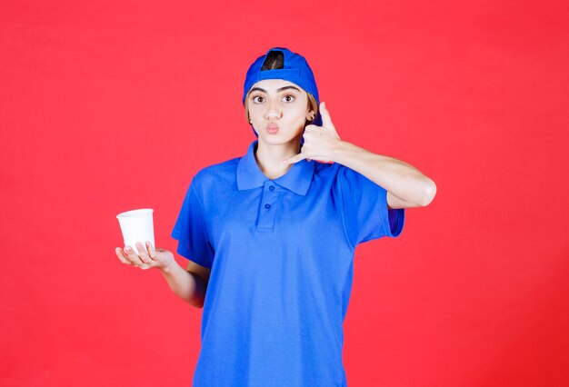 Female service agent in blue uniform holding a disposable cup of drink and asking for a call. 