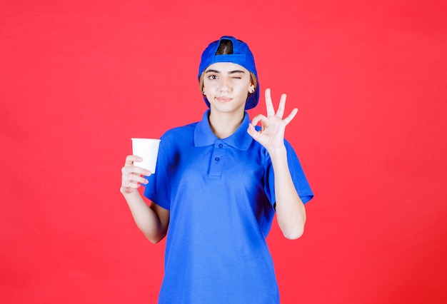 Female service agent in blue uniform holding a disposable cup of drink and enjoying the taste. 