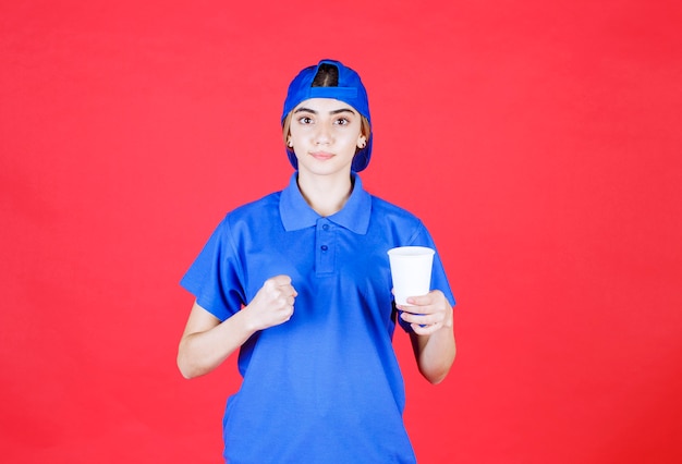 Free photo female service agent in blue uniform holding a disposable cup of drink and showing her fist.