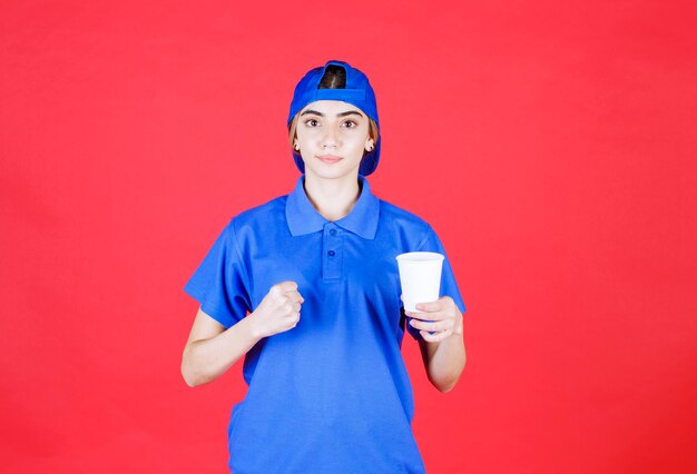 Female service agent in blue uniform holding a disposable cup of drink and showing her fist. 