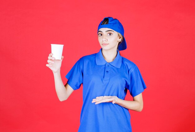 Female service agent in blue uniform holding a disposable cup of drink . 