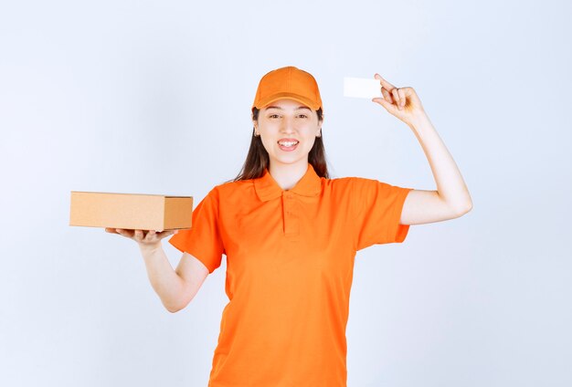 Female service agent in orange color dresscode holding a cardboard box and presenting her business card