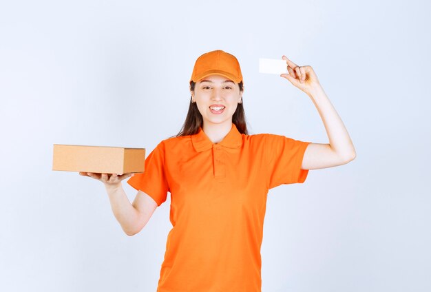 골판지 상자를 들고 그녀의 명함을 제시하는 주황색 드레스 코드의 여성 서비스 요원