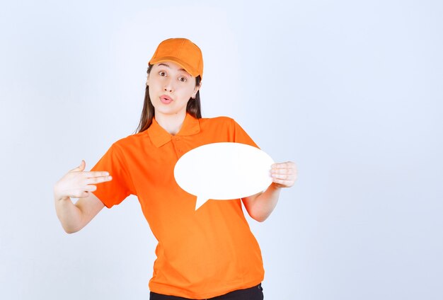 Female service agent in orange color dresscode holding an ovale info board and looks surprized and terrified