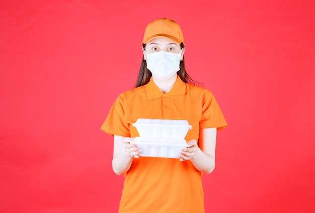 Female service agent in orange color dresscode and mask holding two takeaway food packages