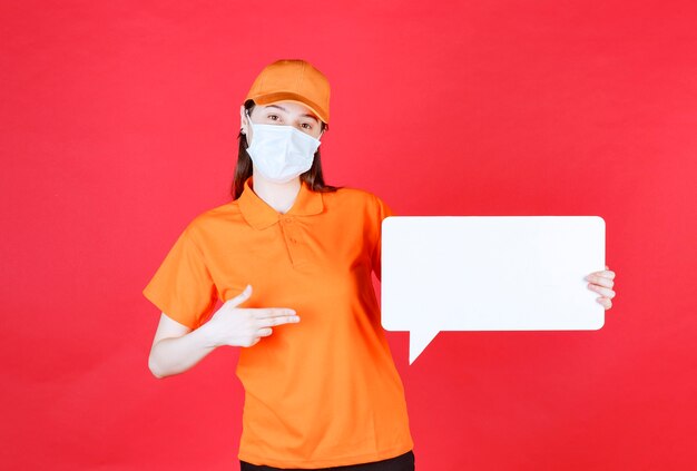 주황색 드레스코드와 흰색 사각형 정보 보드를 들고 있는 마스크를 쓴 여성 서비스 요원
