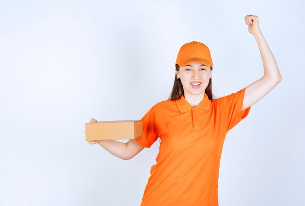 골 판지 상자를 들고 성공적인 손 기호를 보여주는 오렌지 색상 유니폼 여성 서비스 에이전트.