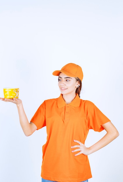 Agente di servizio femminile in uniforme arancione con in mano una tazza gialla da asporto