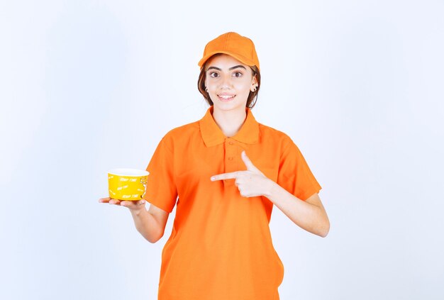 Female service agent in orange uniform holding a yellow takeaway cup